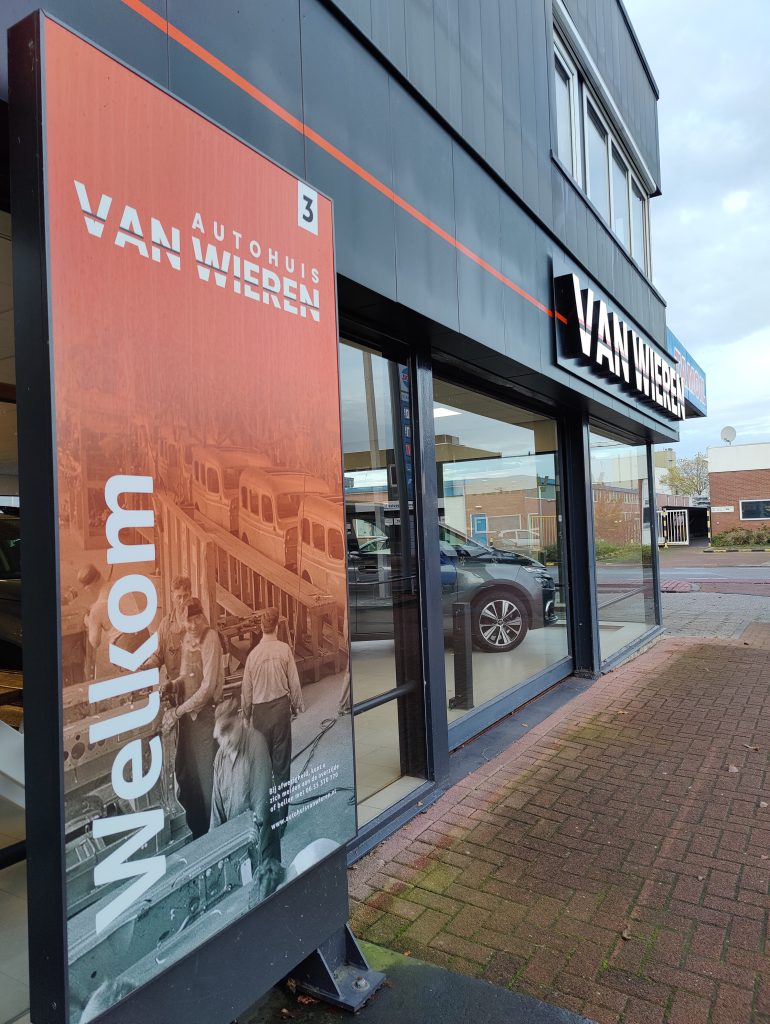 Het welkomstbord met het logo van Autohuis van Wieren voor de gevel met de letters VAN WIEREN